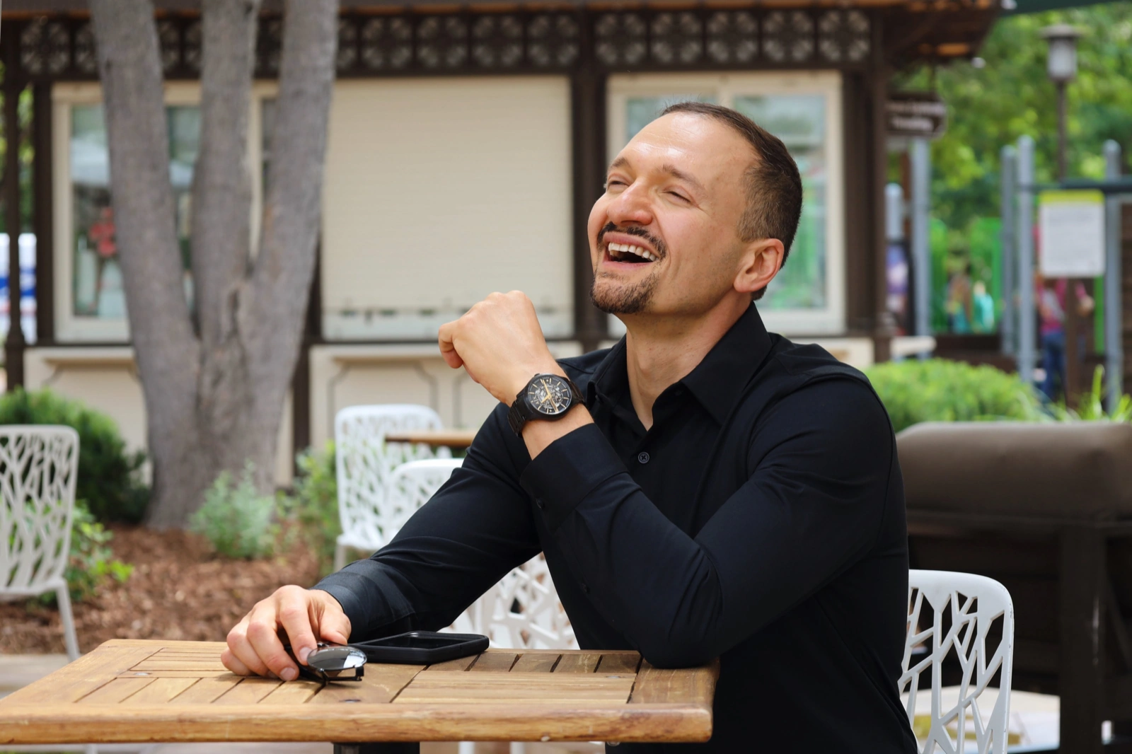 Male poses in action: man laughing at an outdoor cafe table in a black shirt
