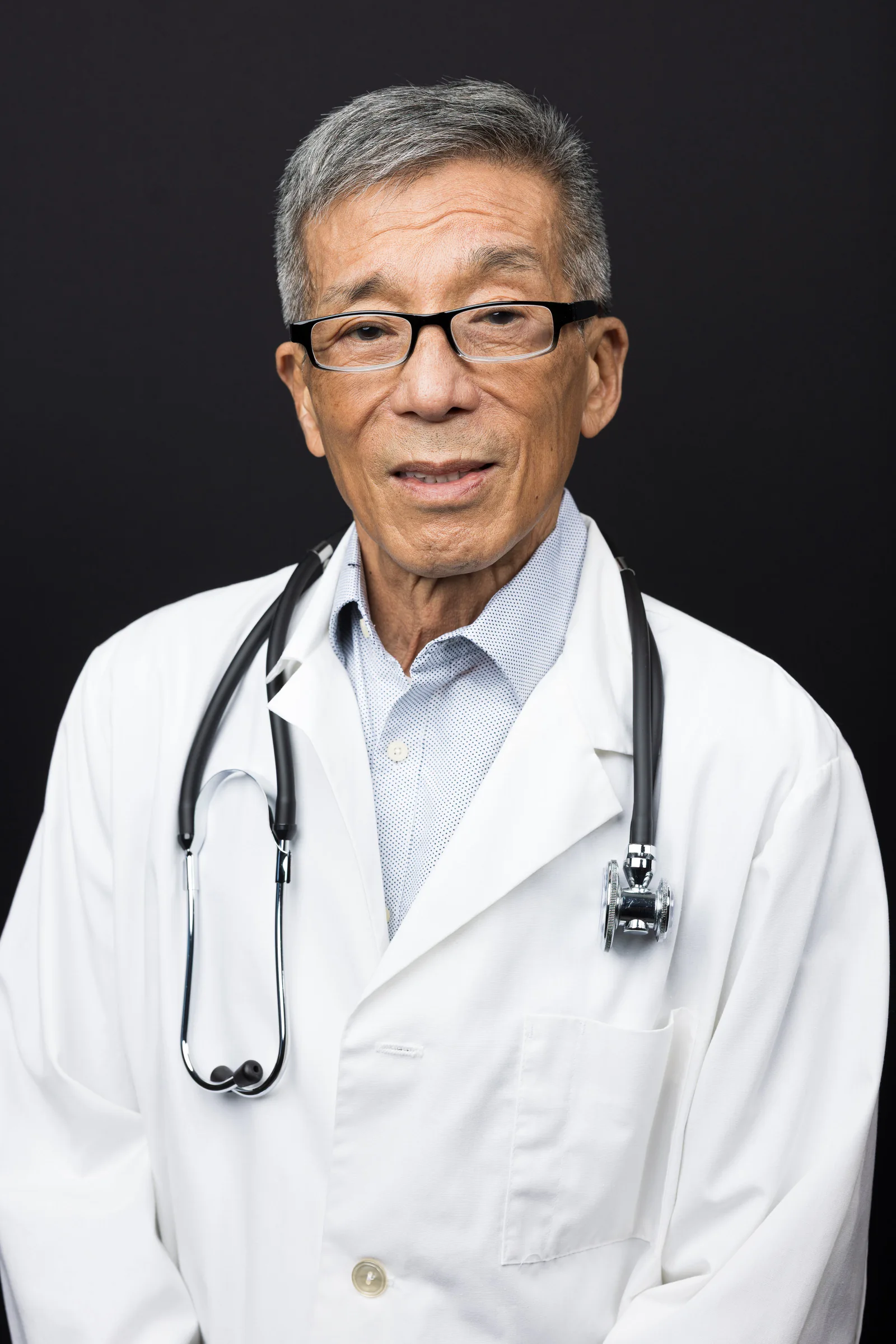 Doctor headshots: older physician in a white coat and stethoscope on a black backdrop