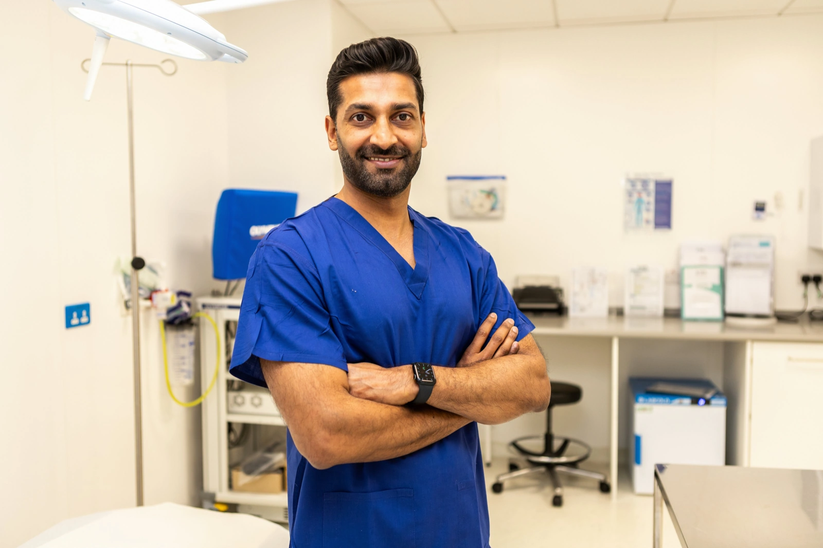 Doctor headshots in scrubs: provider with folded arms in a bright clinic treatment room