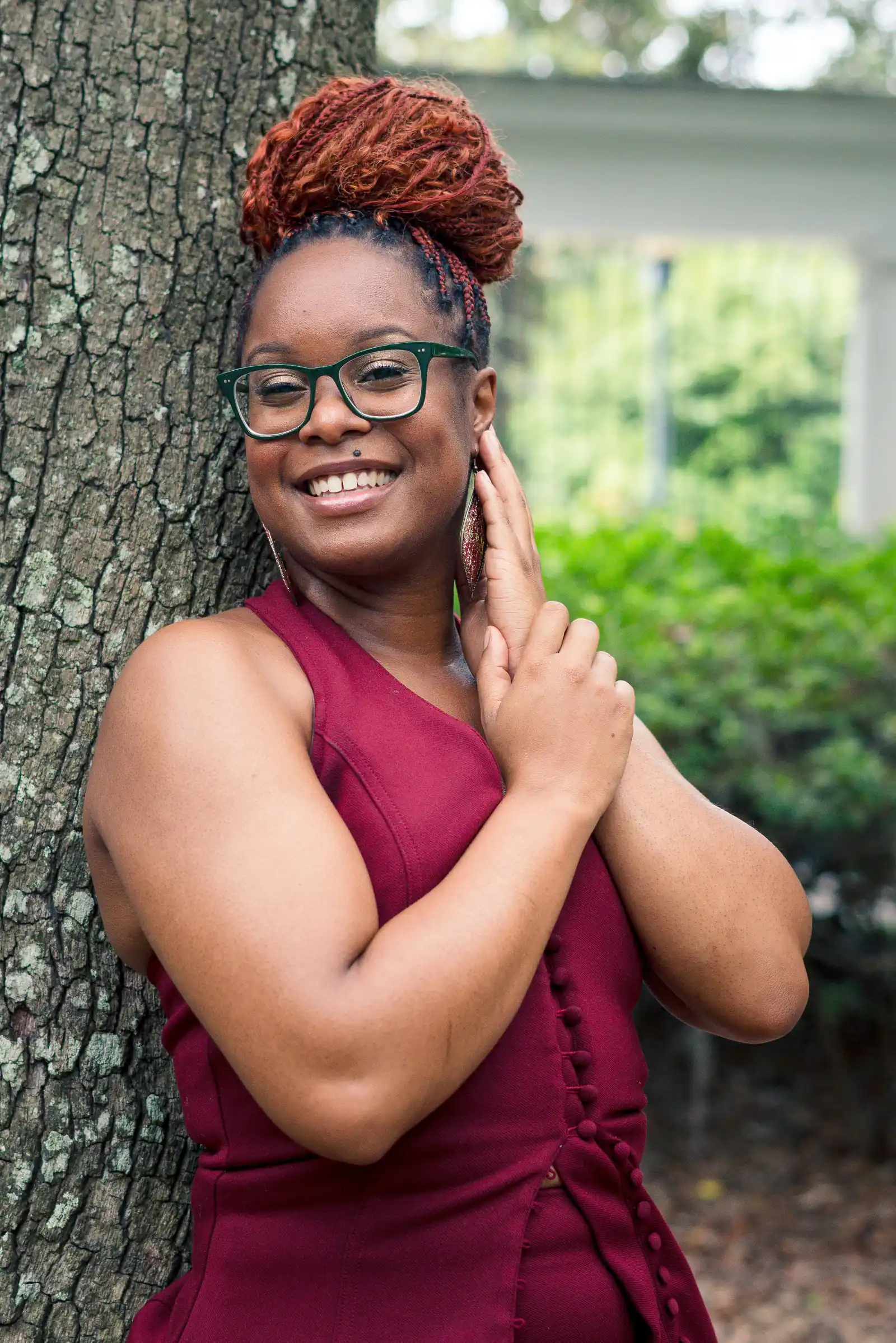 Poses for women: soft hands raised to the face, smiling against a tree trunk