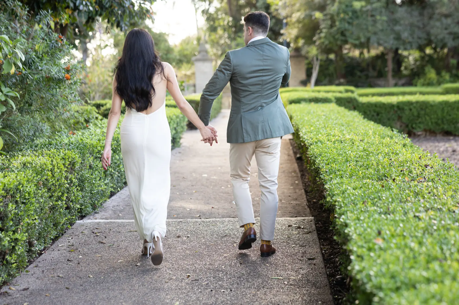 Walking couple poses: hand in hand down a garden path between hedges