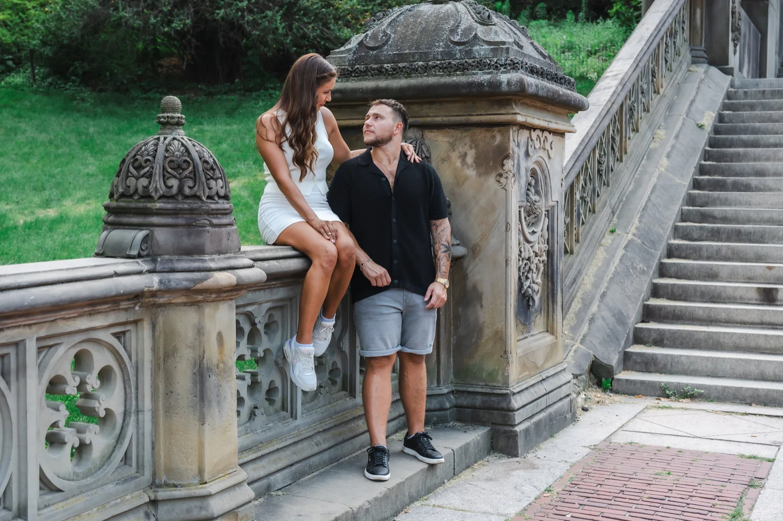Couple poses for a height difference: one partner sits on a stone ledge