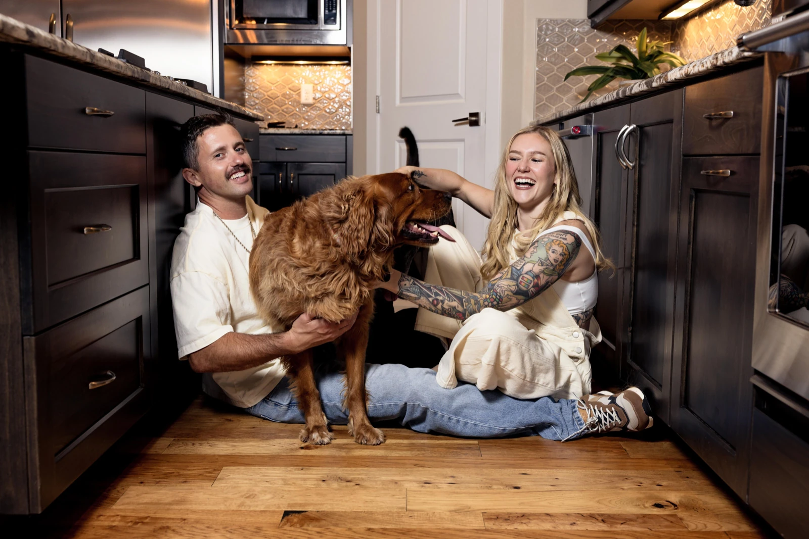 At-home couple poses: laughing on the kitchen floor with their dog