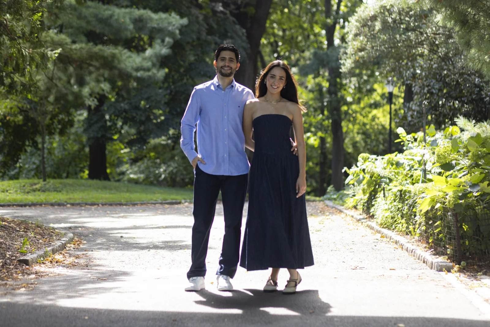 Couple poses in coordinated blue and navy outfits on a tree-lined path