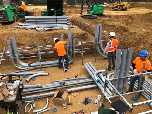 Electricians installing conduit in a pit before concrete is poured