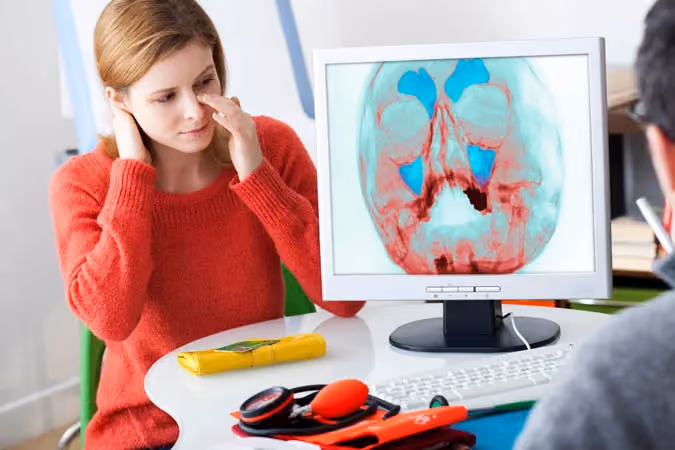 Person in red sweater discussing a cranial X-ray image on a computer screen with another individual.