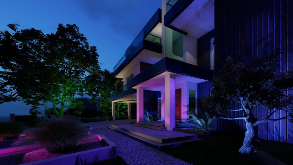 The same entry corner with columns washed lavender and pink, one tree uplit green and another cool white, and planting beds in magenta
