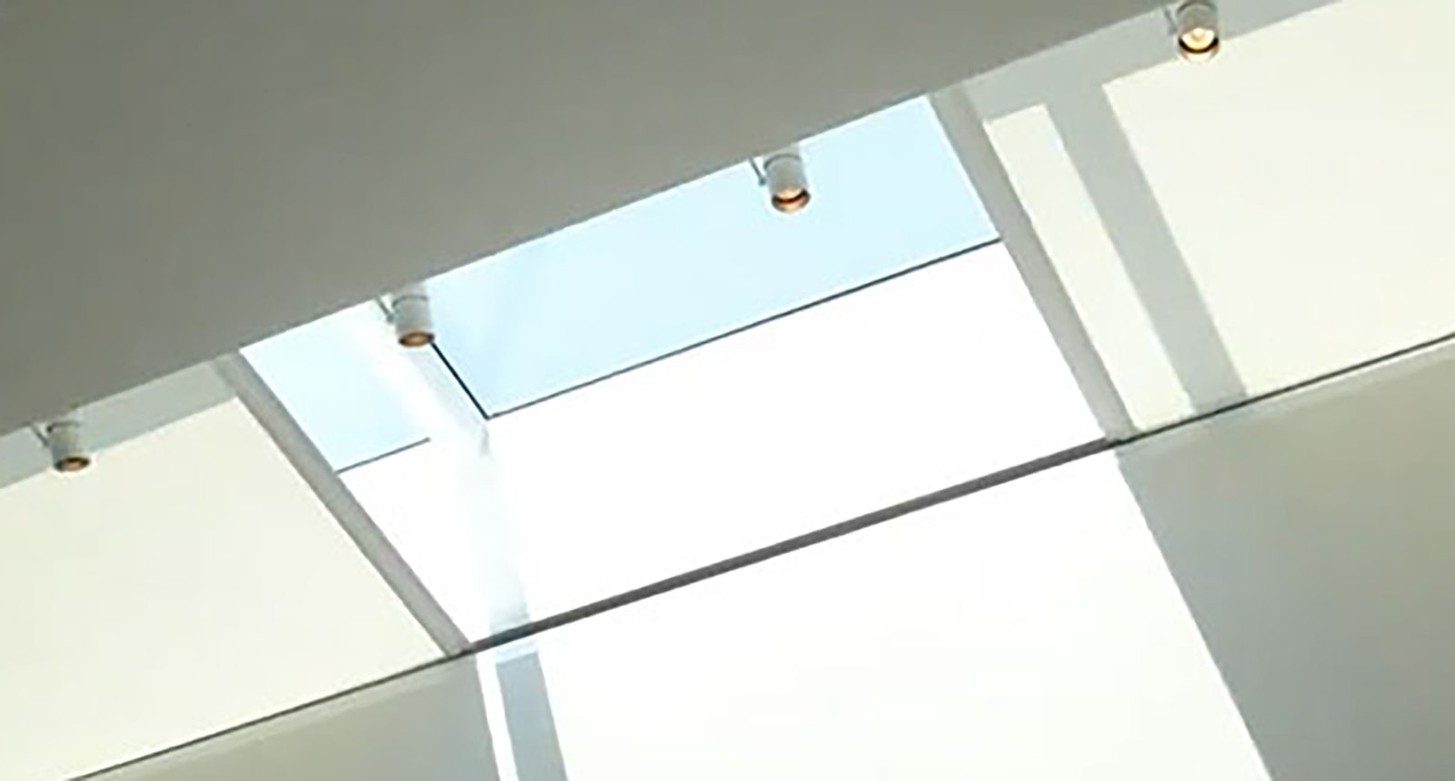 Sloped ceiling with skylight openings and white tensioned fabric partly drawn across them, small white track spots