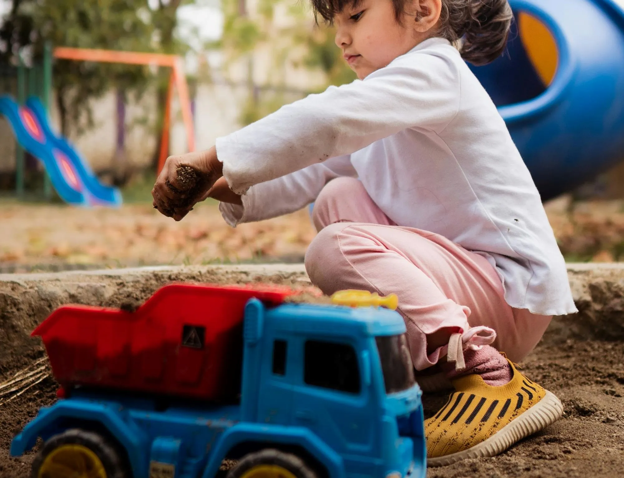 A little girl playing with a toy truck in the mud