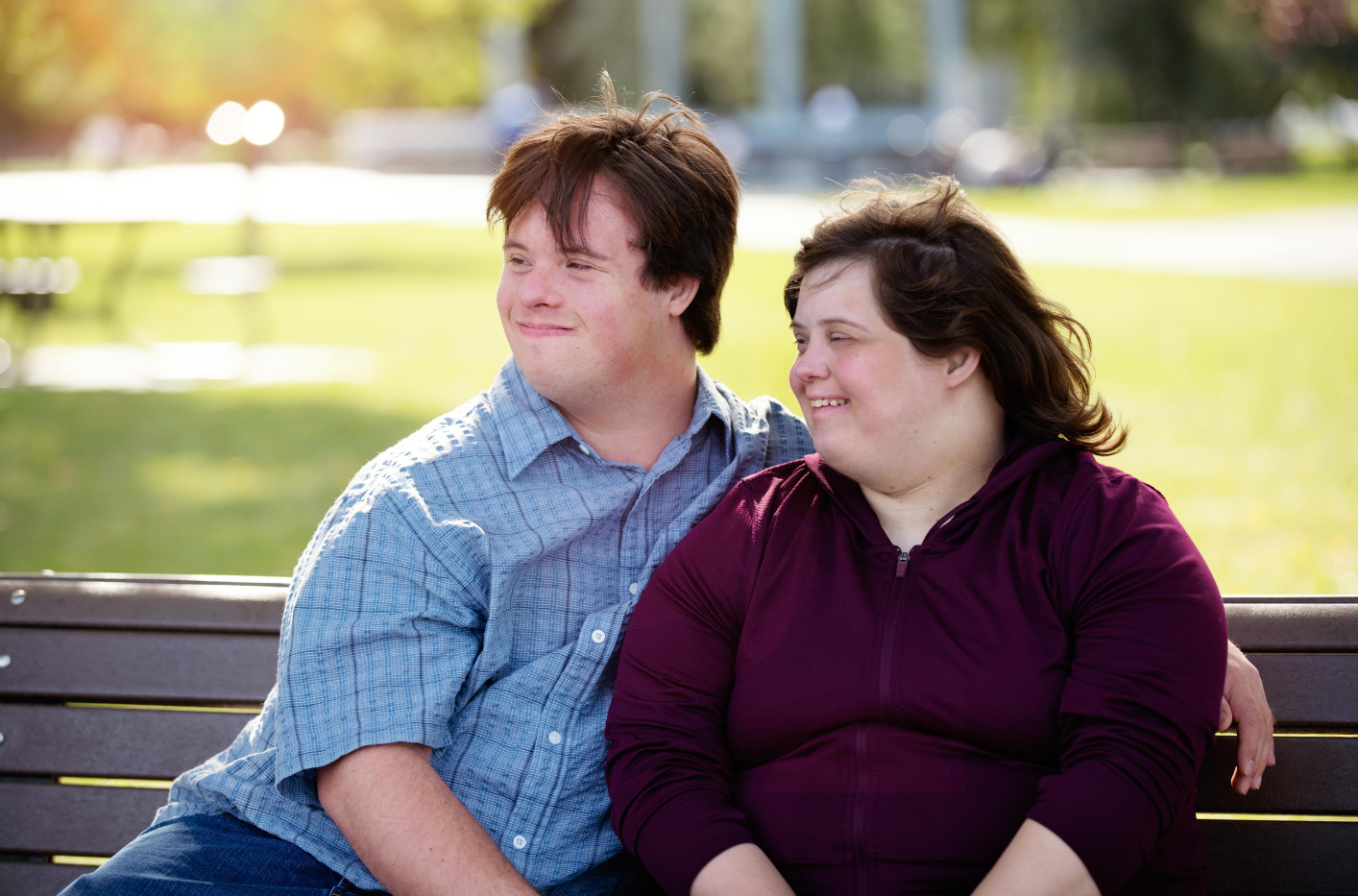 A young disabled couple sitting on a park bench with their arms around one another