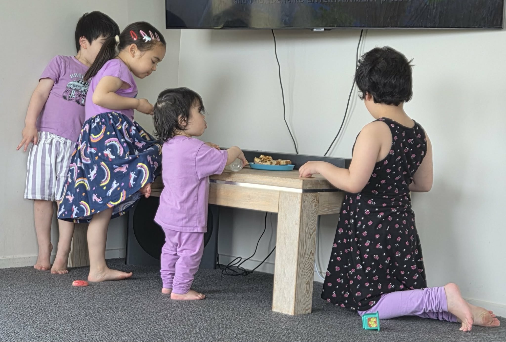 A picture of four sibings, two daughters and two sons, eating at a snack table together in front of a tv.