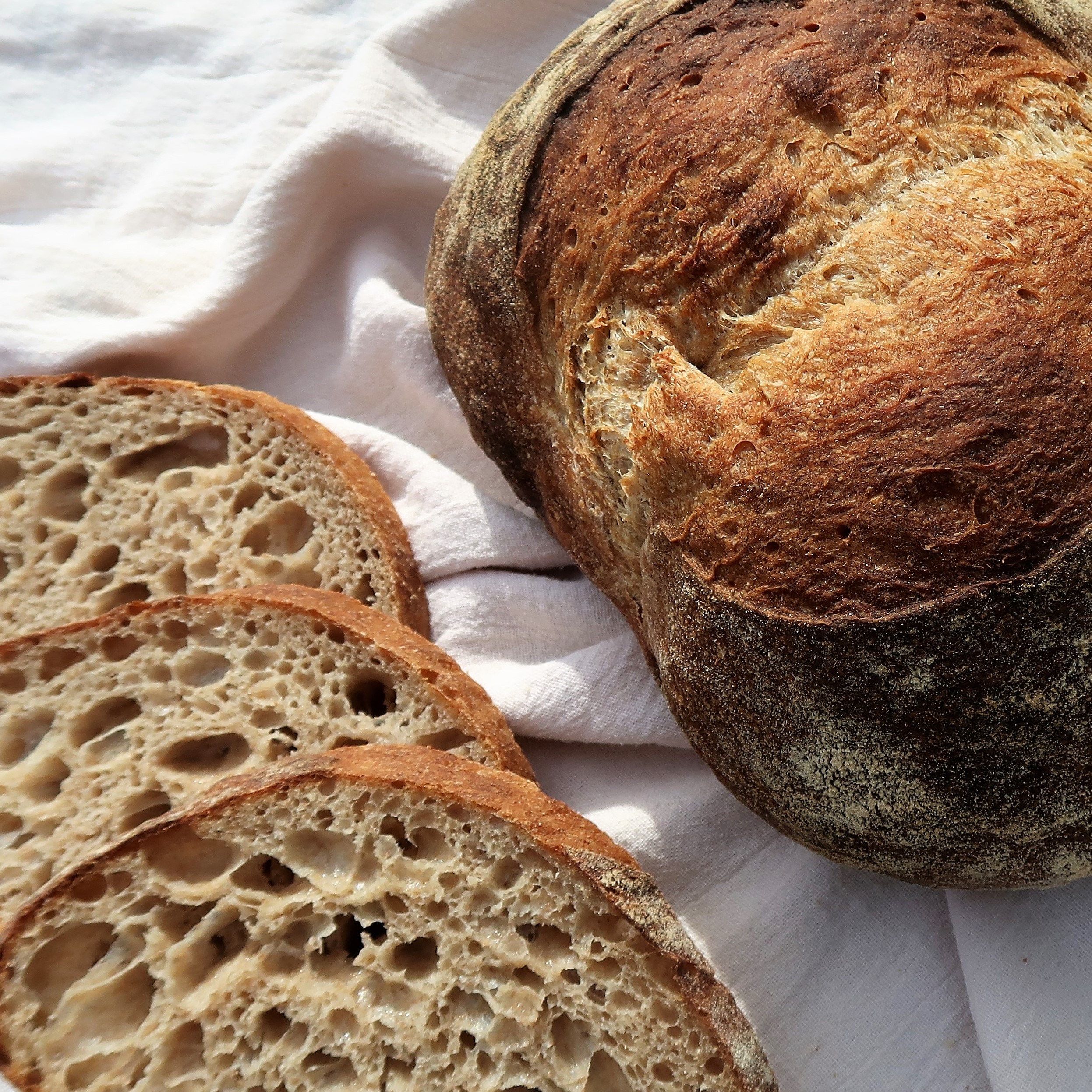 A golden, crispy loaf of sourdough sits beside a few slices of bread