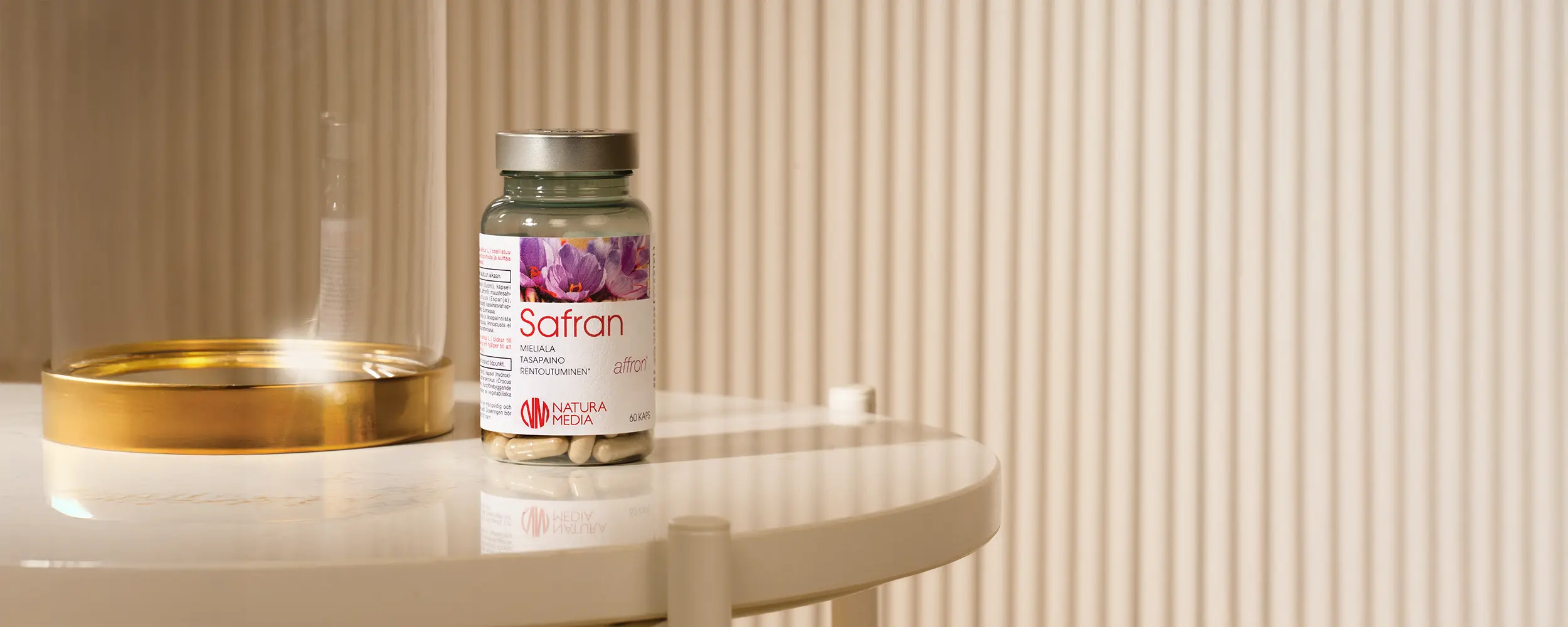 Natura Median Safran-purkki vaalean beigellä pöydällä, taustalla näkyy himmeänä beigeä rimaseinää. Purkin vieressä pöydällä on lasinen kupu messinginvärisellä alustalla.