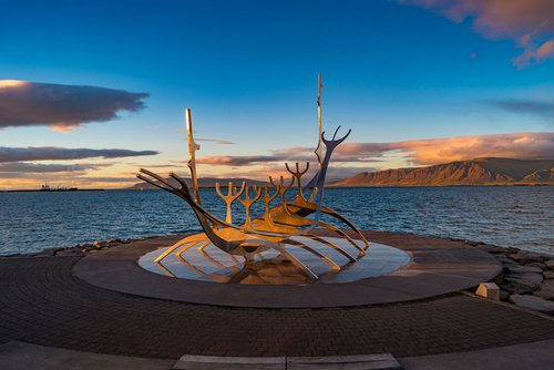 Cityscape over Reykjavik business and touristic downtown, embankment, ocean, harbor, modern buildings and monument of Viking boat Sun Voyager at sunset skyline
