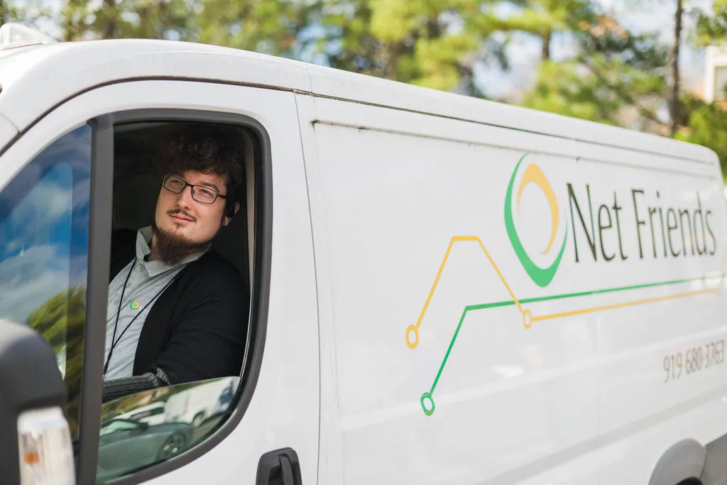 Man with glasses and a beard sitting in the driver's seat of a white van with Net Friends logo on the side.