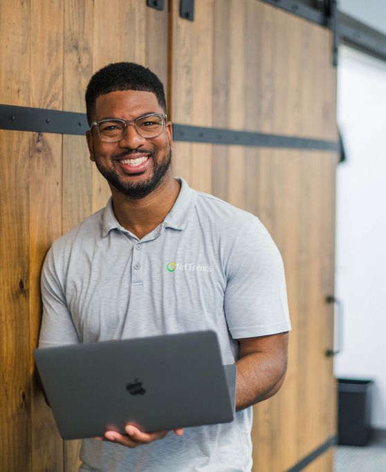 IT Tech leaning against wooden door holding macbook