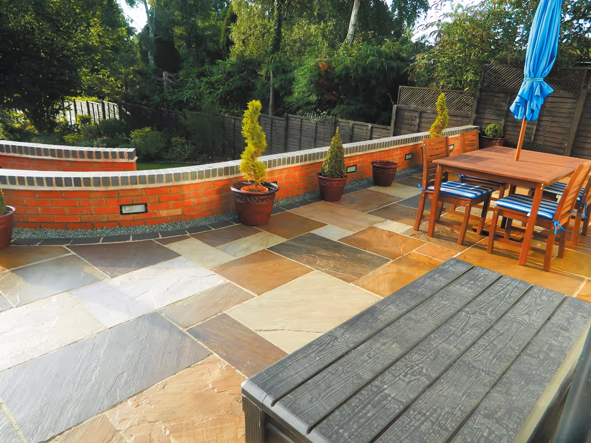 Mixed size camal natural stone patio with large charcoal rumbled block, large red retaining wall with blue engineering brick - angle 1