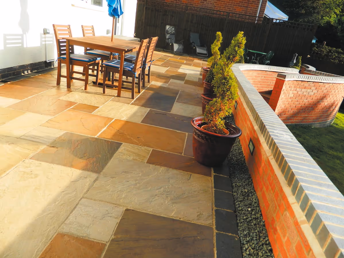 Mixed size camal natural stone patio with large charcoal rumbled block, large red retaining wall with blue engineering brick - angle 3