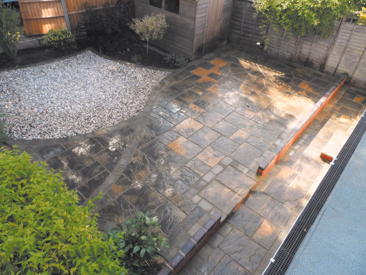 Winter stone concrete patio with matching circle, patio edged with large charcoal rumbled block, red walling finished with blue engineering brick.