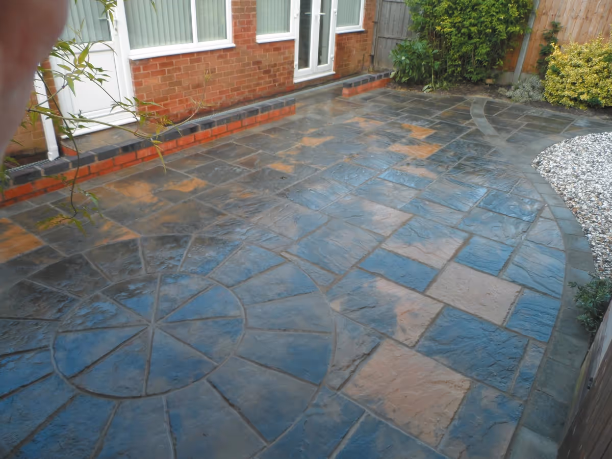 Winter stone concrete patio with matching circle, patio edged with large charcoal rumbled block, red walling finished with blue engineering brick and new lawn - angle 4