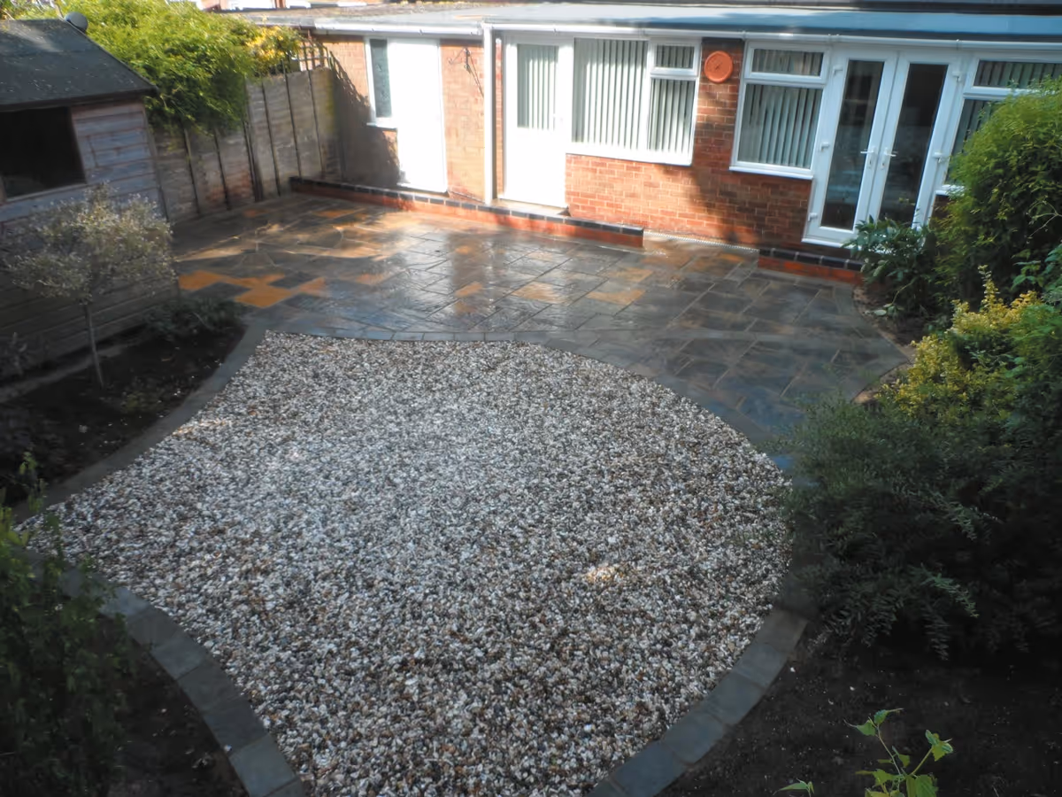 Winter stone concrete patio with matching circle, patio edged with large charcoal rumbled block, red walling finished with blue engineering brick and new lawn - angle 1