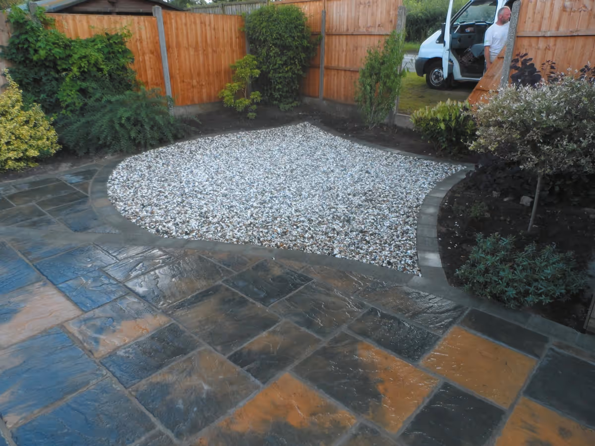 Winter stone concrete patio with matching circle, patio edged with large charcoal rumbled block, red walling finished with blue engineering brick and new lawn - angle 5