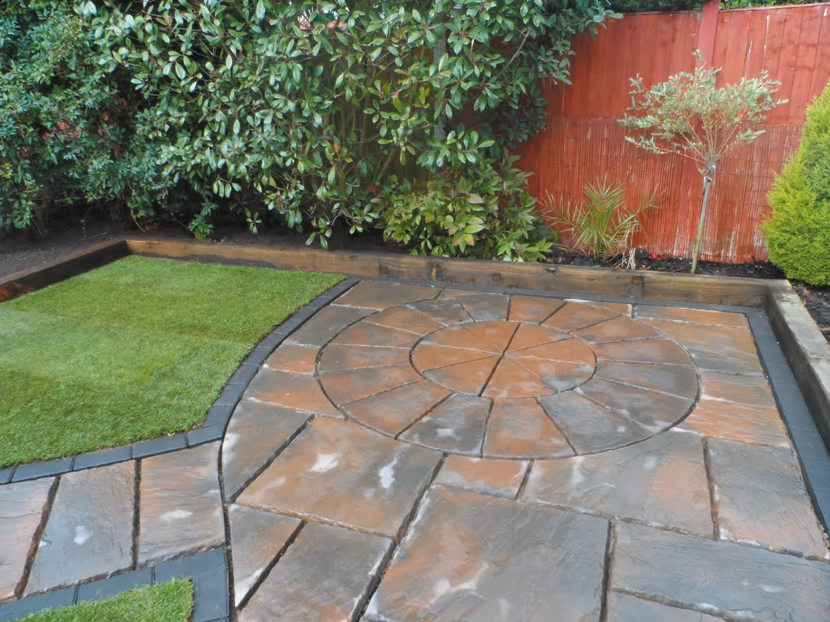 Two size autumn gold concrete patio with matching circle, patio edged with standard charcoal blocks, retaining sleeper beds and new lawn - angle 1