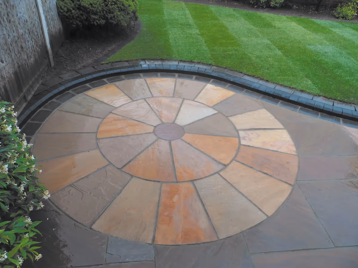 Mixed size camal natural stone patio with natural stone circle, edged with small sets and large charcoal rumbled block. 