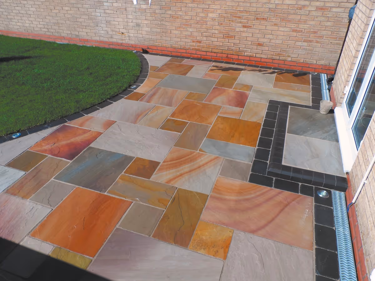 Mixed size camal natural stone patio with large charcoal rumbled block and step built from small key set kerbs