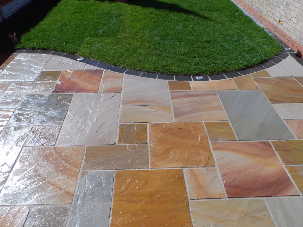 Mixed size camal natural stone patio with large charcoal rumbled block and step built from small key set kerbs - angle 5