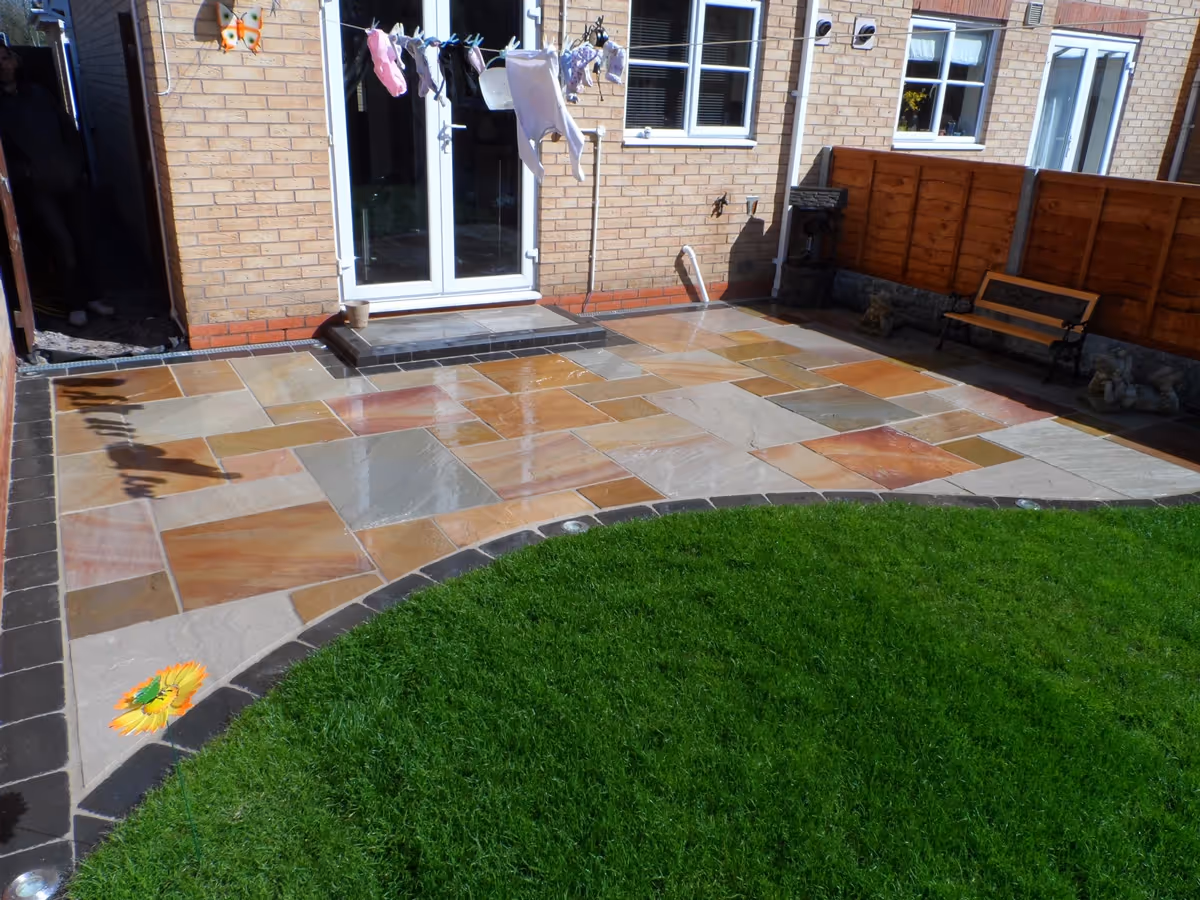 Mixed size camal natural stone patio with large charcoal rumbled block and step built from small key set kerbs - angle 3