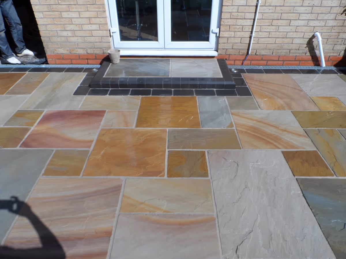 Mixed size camal natural stone patio with large charcoal rumbled block and step built from small key set kerbs - angle 4