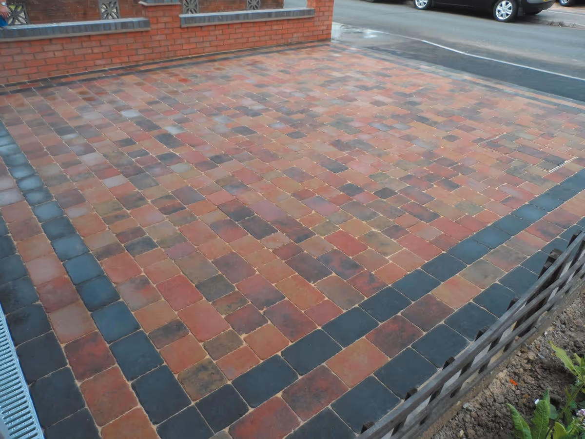 Orchid flame Rumbled paving set driveway with triple borders using charcoal, boundary wall installed and an ACO channel drainage system - angle 1