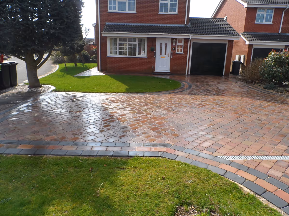 Autumn mix Rumbled paving set driveway with a triple border in charcoal, ACO channel drainage system and new lawn areas using Rolawn medallion turf - angle 1