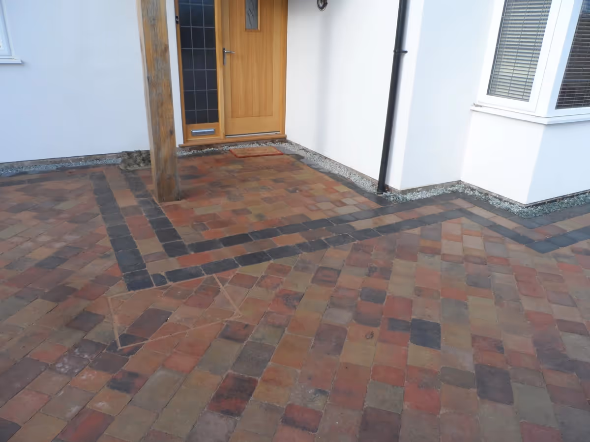 Orchid flame Rumbled paving set large driveway with a triple border using Charcoal, K.S kerb set lawn retainer, and an inset manhole tray- angle 1