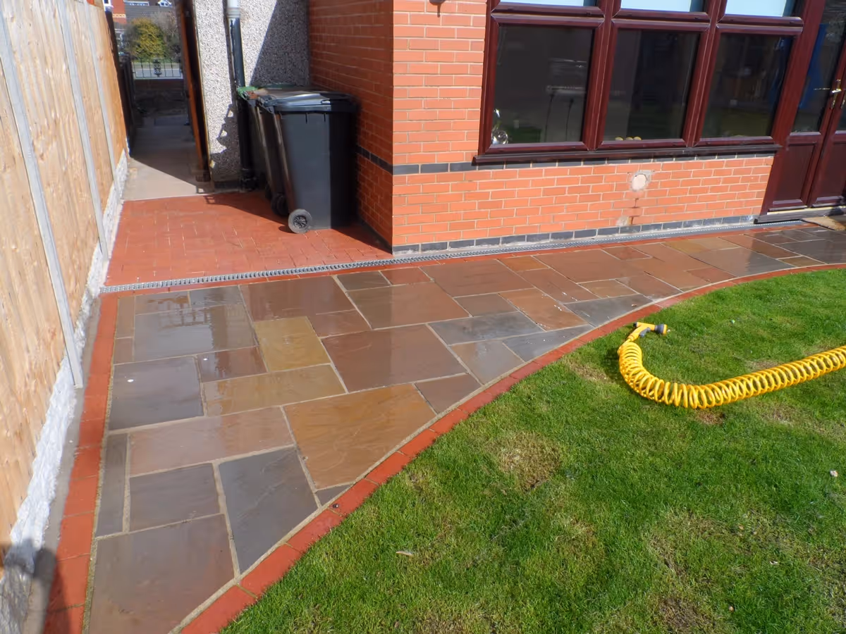 Mixed size camal natural stone patio with red standard blocks. Red standard block paving with standard charcoal block border - angle 1