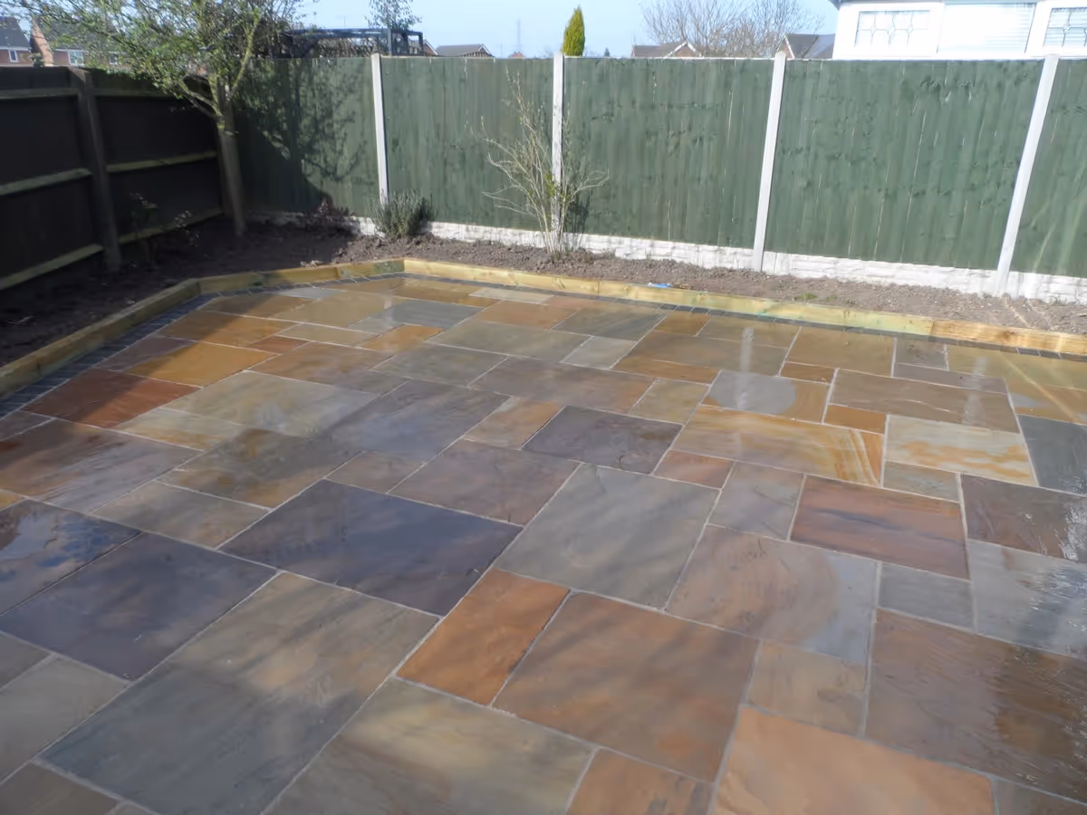 Mixed size camal natural stone patio with large charcoal rumbled block and sleeper planter - angle 1