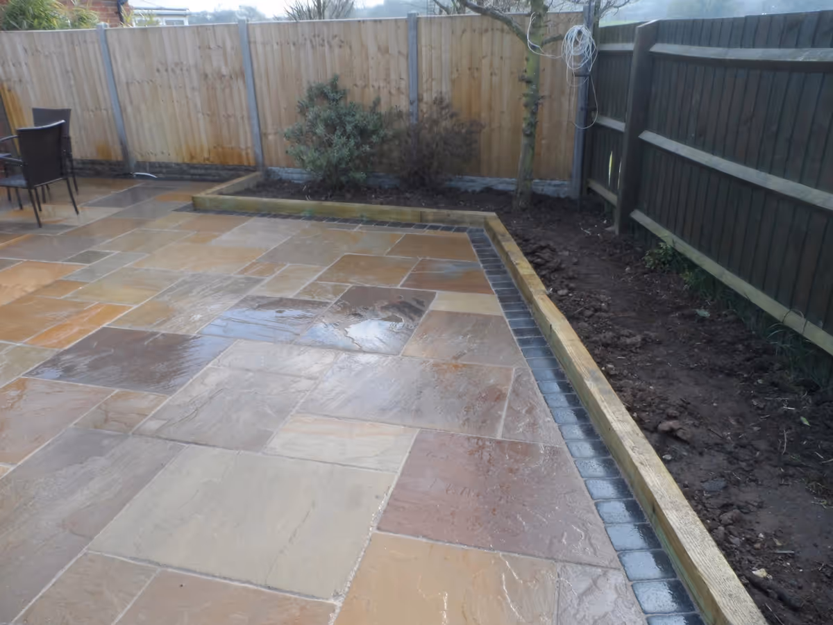 Mixed size camal natural stone patio with large charcoal rumbled block and sleeper planter - angle 2
