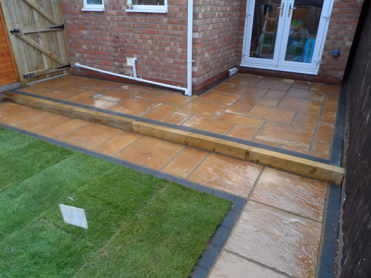 Two size autumn gold concrete patio with standard charcoal block, sleeper step, new lawn and treated lap fence panels with concrete posts and gravel boards - angle 2