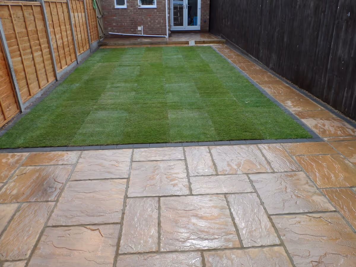 Two size autumn gold concrete patio with standard charcoal block, sleeper step, new lawn and treated lap fence panels with concrete posts and gravel boards - angle 4