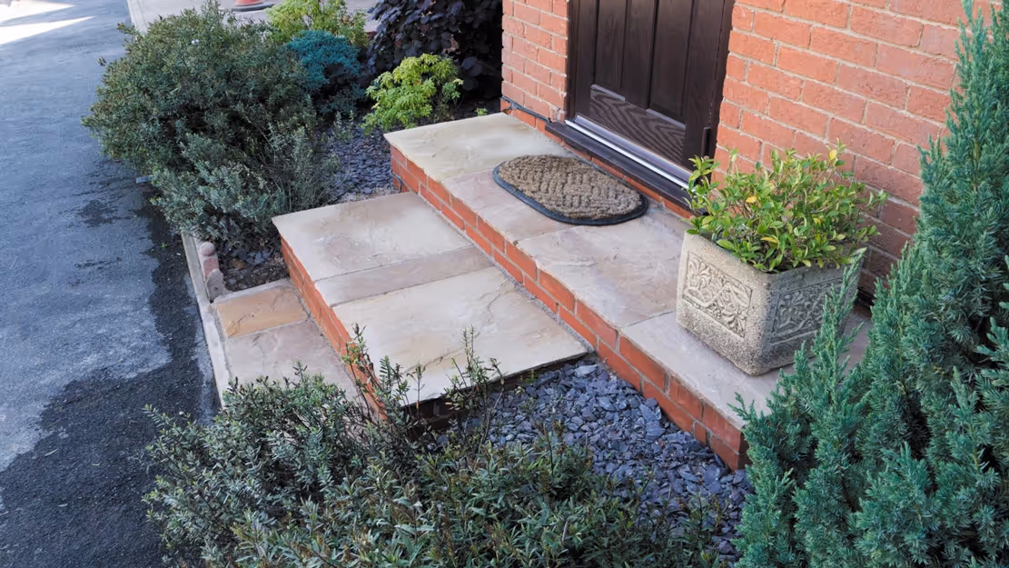 Mixed size camal natural stone patio with three size charcoal rumbled block, red brick wall and steps finished with camal copings - angle 4