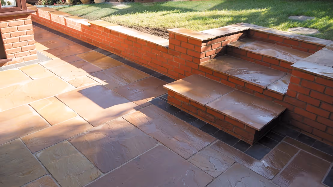 Mixed size camal natural stone patio with three size charcoal rumbled block, red brick wall and steps finished with camal copings - angle 1