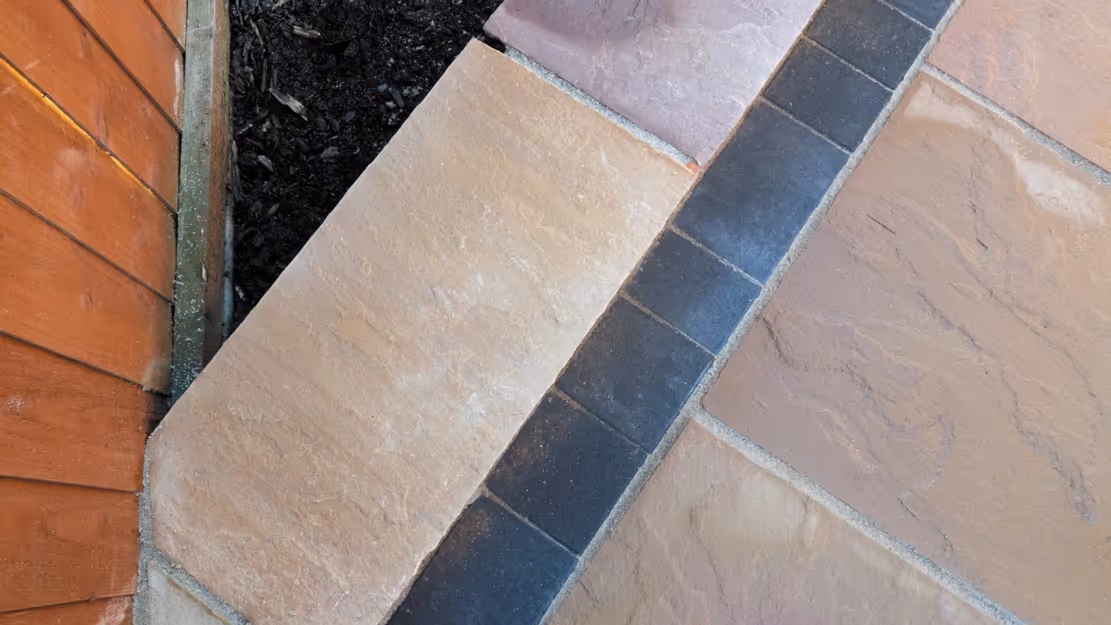 Mixed size camal natural stone patio with three size charcoal rumbled block, red brick wall and steps finished with camal copings - angle 6