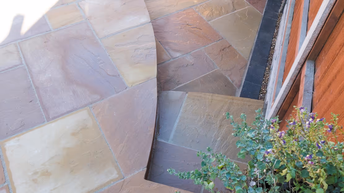 Mixed size camal natural stone patio with three size charcoal rumbled block, red brick wall and steps finished with camal copings - angle 5