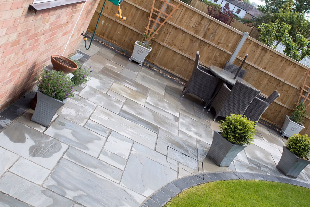 Mixed size grey natural size patio with large charcoal rumbled block, sleeper planter area and small kerb edging