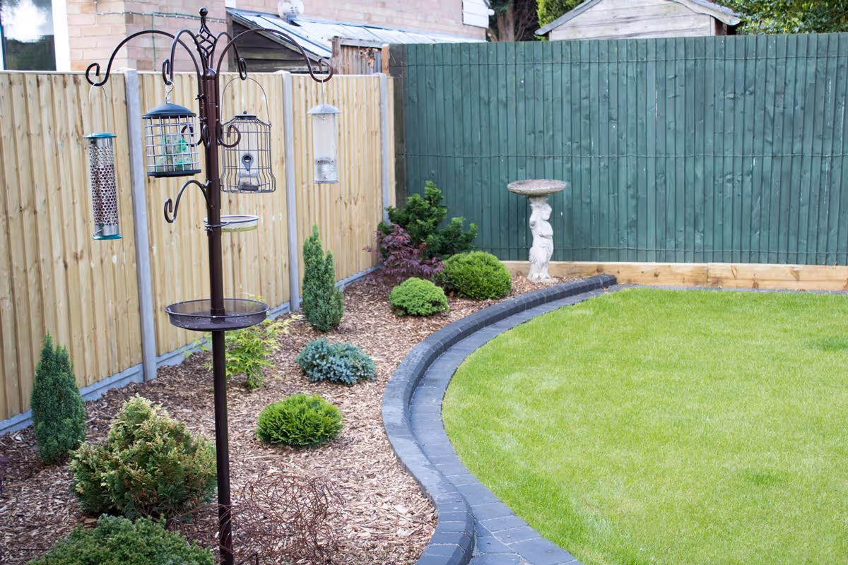 Mixed size grey natural size patio with large charcoal rumbled block, sleeper planter area and small kerb edging - angle 2