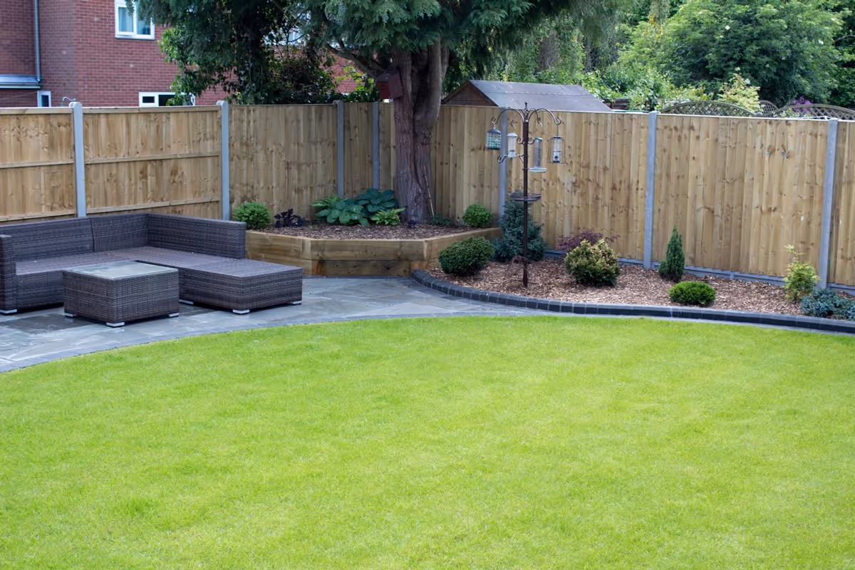 Mixed size grey natural size patio with large charcoal rumbled block, sleeper planter area and small kerb edging - angle 1