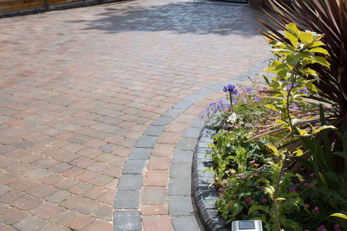 Autumn mix Rumbled paving set driveway with triple border in charcoal, raised planter using K.S kerb sets, ACO channel drainage system installed and new iron gates - angle 2