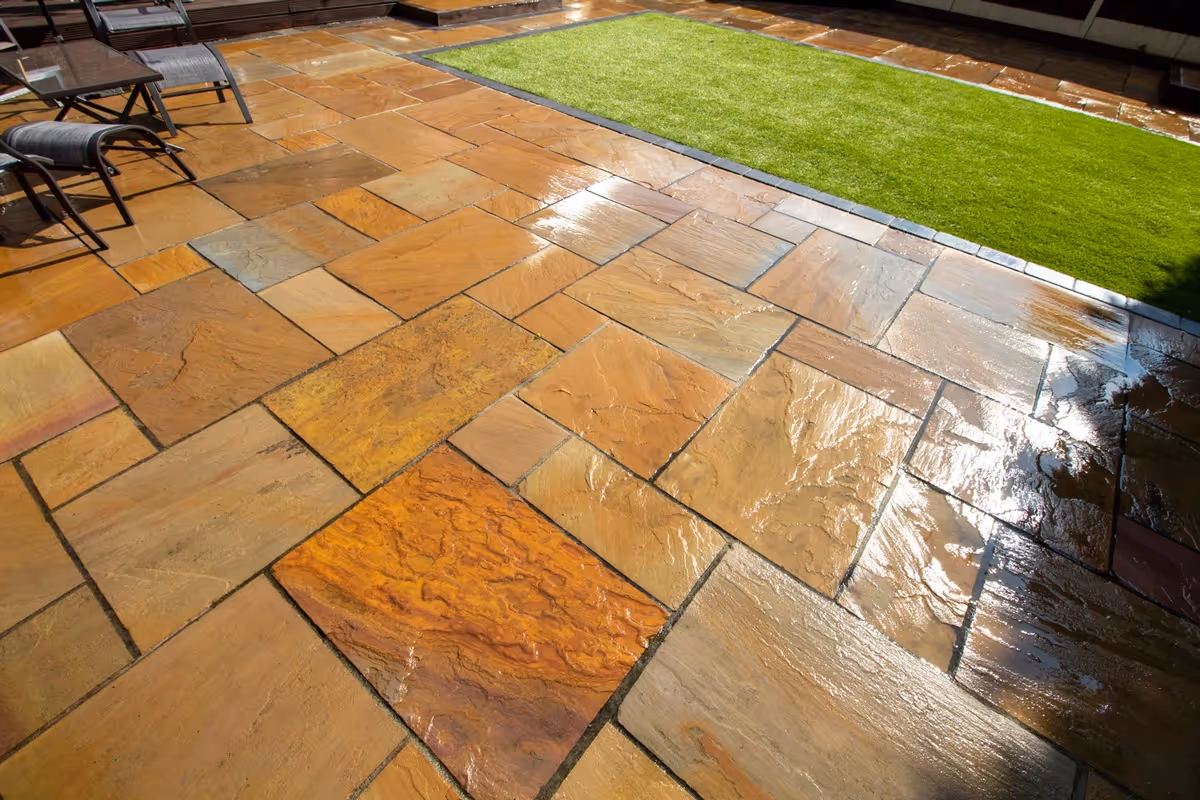 Mixed size camal natural stone patio with large charcoal rumbled block, raised sleeper area and artificial grass lawn.  - angle 6