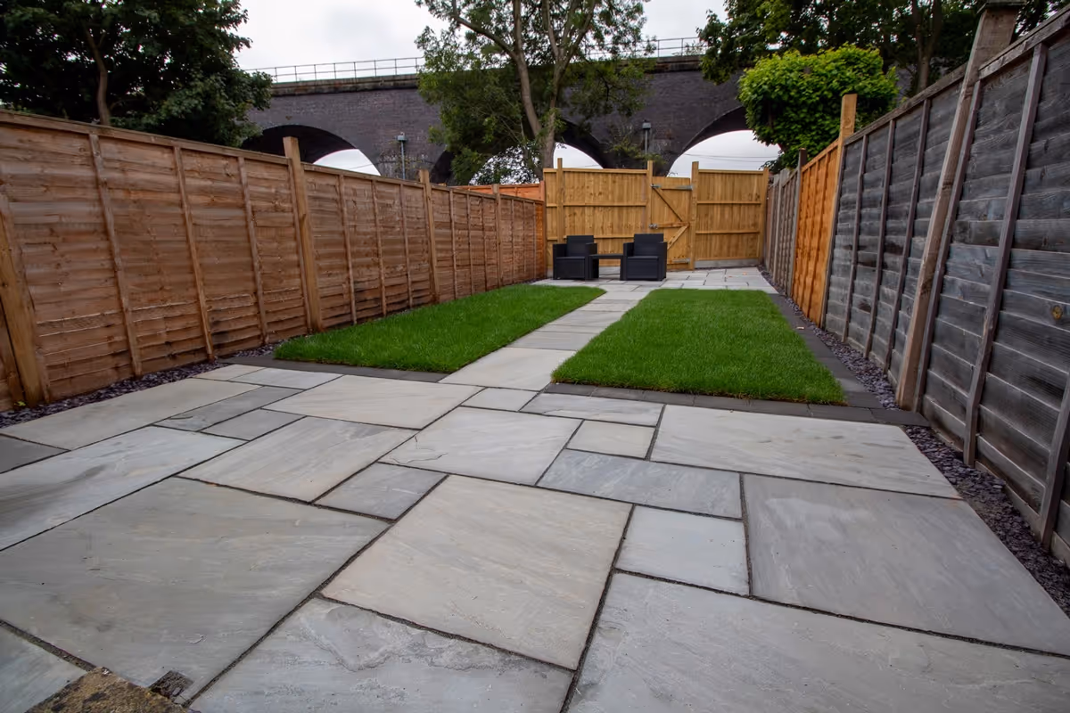 Kandla Grey, Natural Stone slabs with a Granite Resin based jointing compound. Aged effect large Charcoal Paver around perimeters. Rowland Medallion real turf. Concrete boards fitted together with Feather Edge Fence Panels and Gate. Plum slate decorative stones.